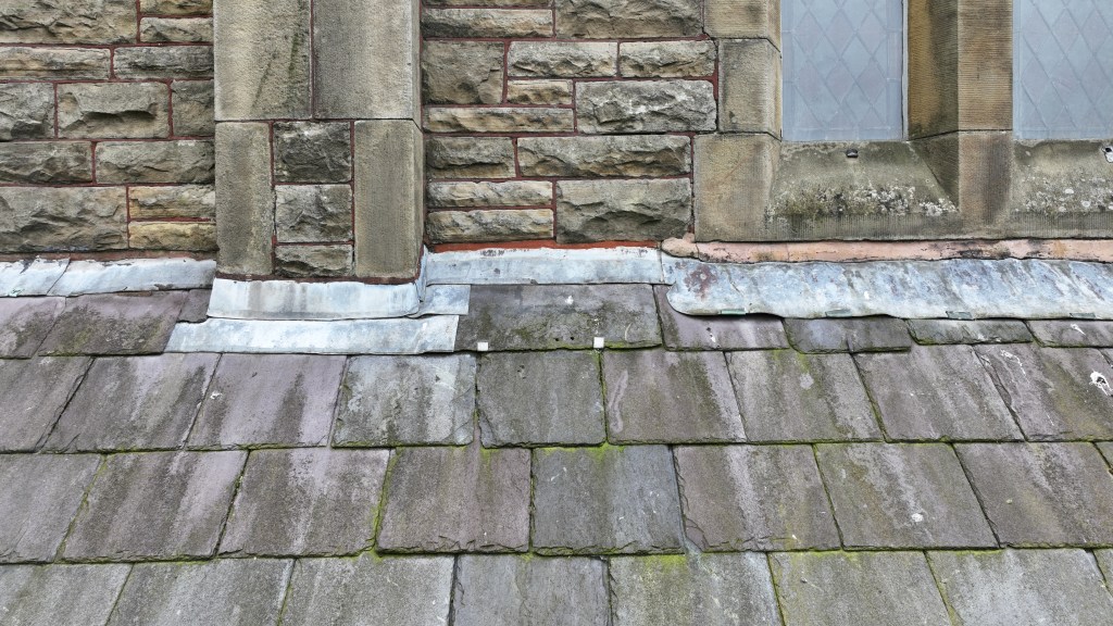 Close-up of a building's roof, showcasing stonework, slate tiles, and metal flashing.